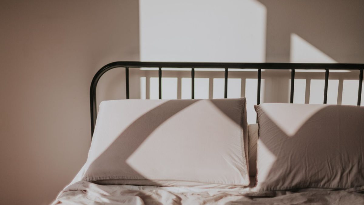 Two blush pillows on a made bed with the last of the evening sun across them